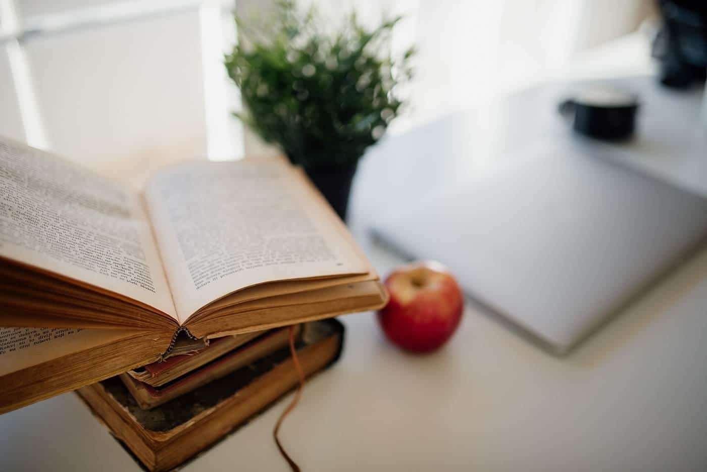 An open book, an apple and a laptop on a bright desk