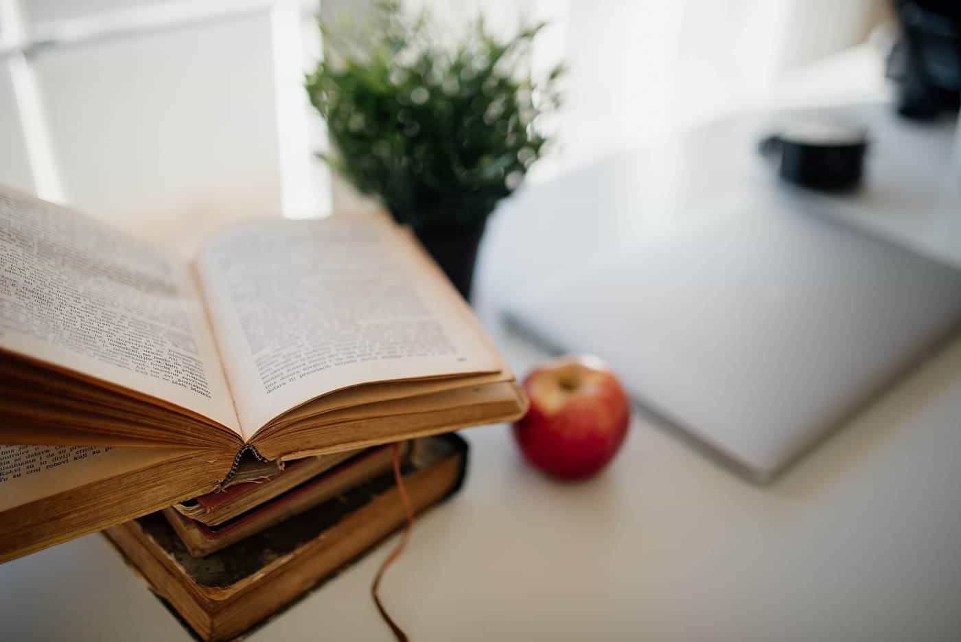 An open book, an apple and a laptop on a bright desk
